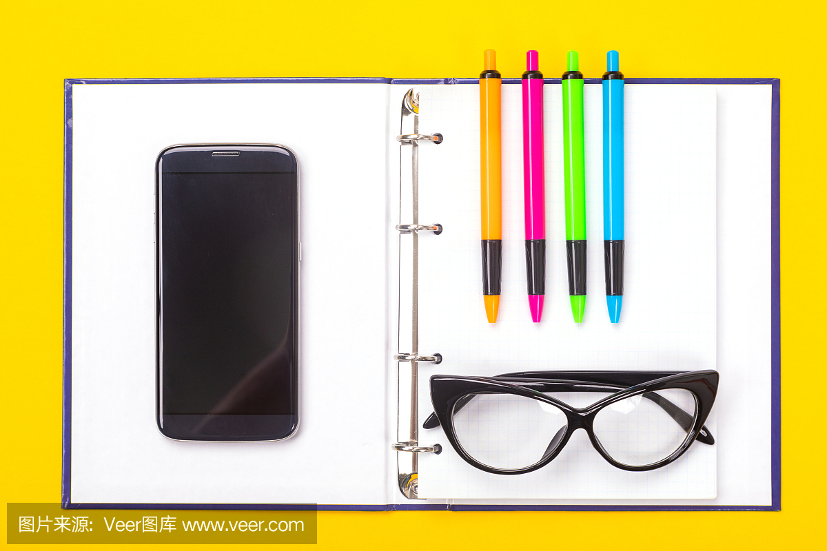 俯视图的工作空间桌子与笔记本,眼镜和彩色笔孤立在黄色背景